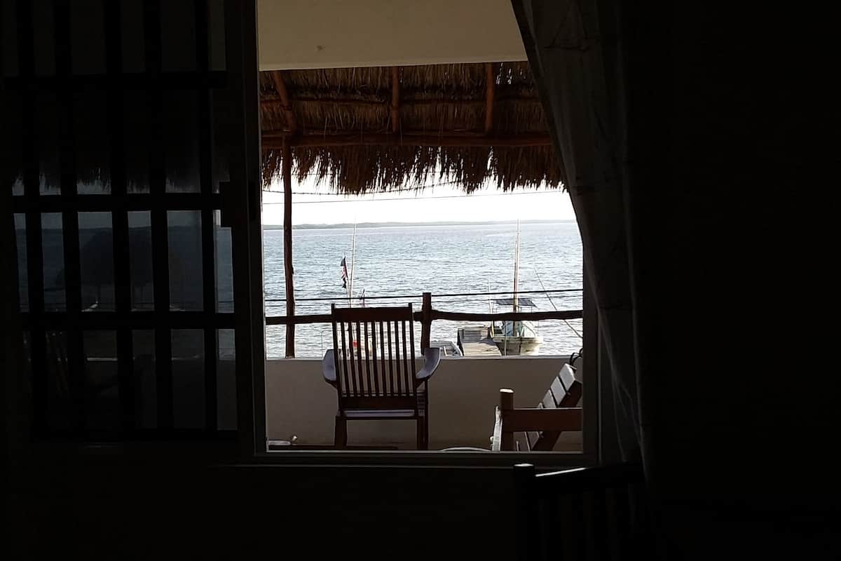 A balcony with a view of the sea, a chair, and a table with a plant.