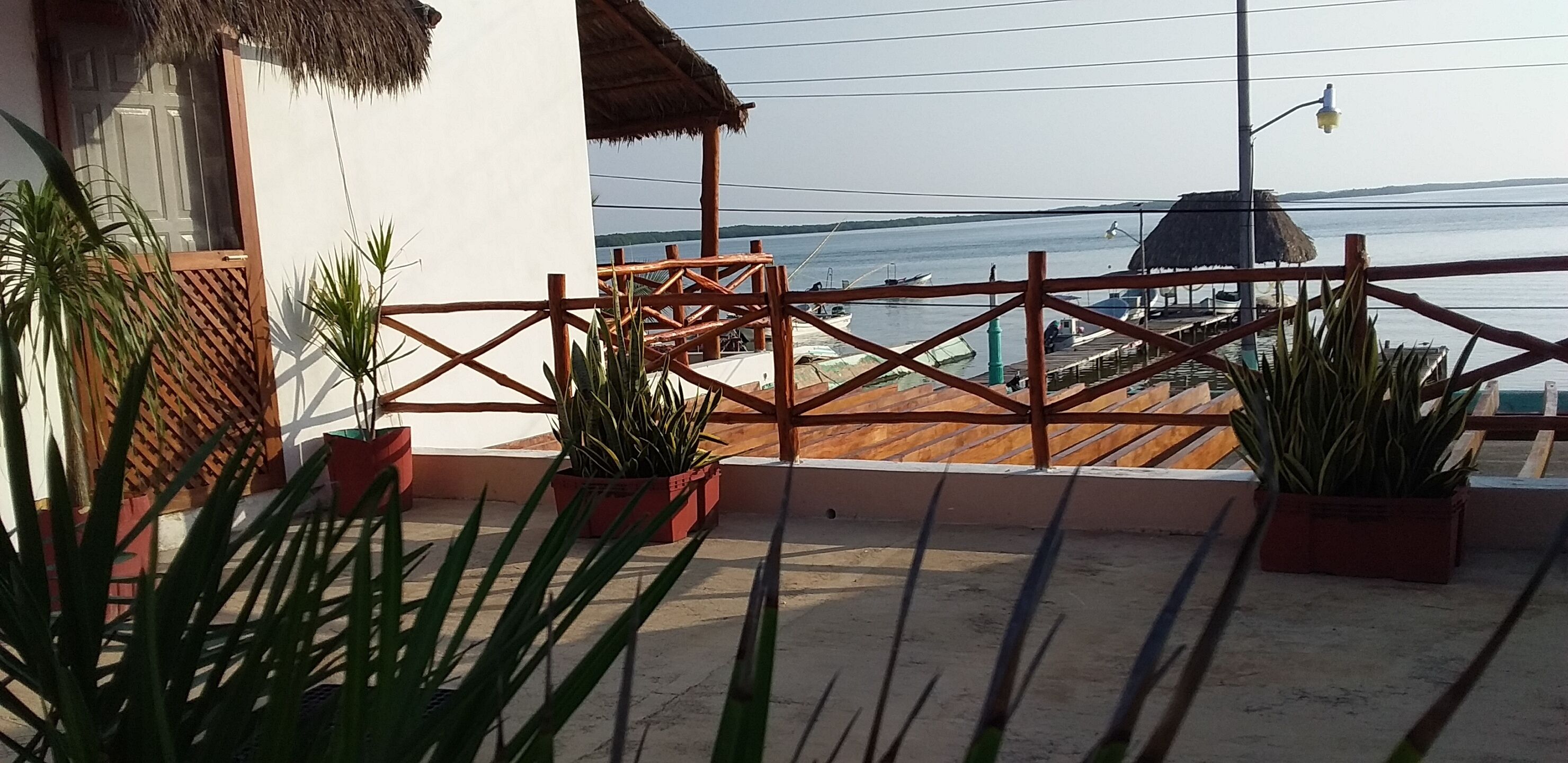 Un balcon agrémenté de plantes en pot, une clôture en bois et une vue sur la mer et les bateaux.