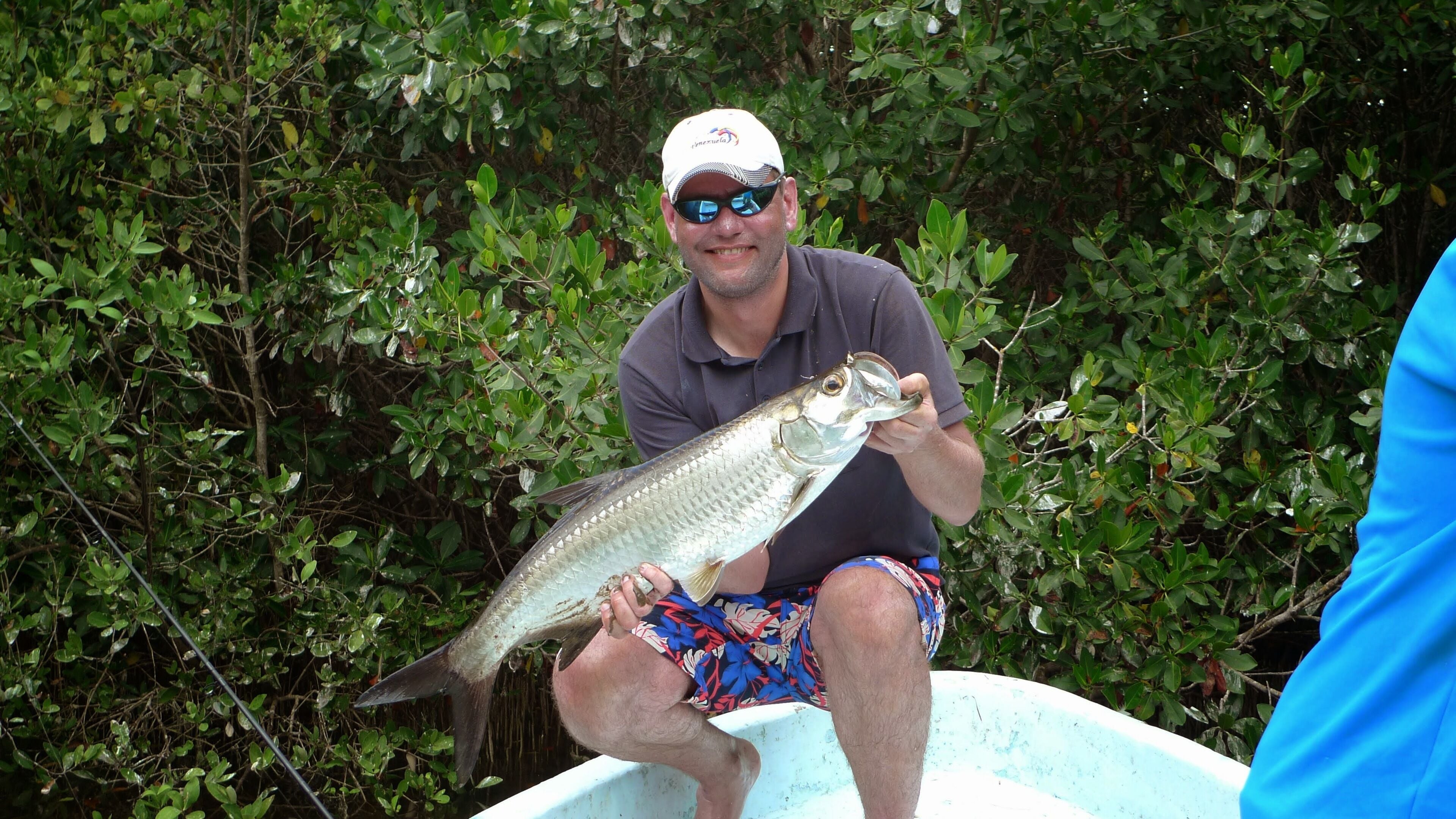 A person holding a fish in a boat surrounded by dense green foliage.