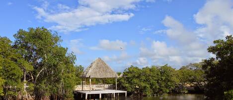 A thatched-roof structure on stilts over calm water, surrounded by dense greenery.