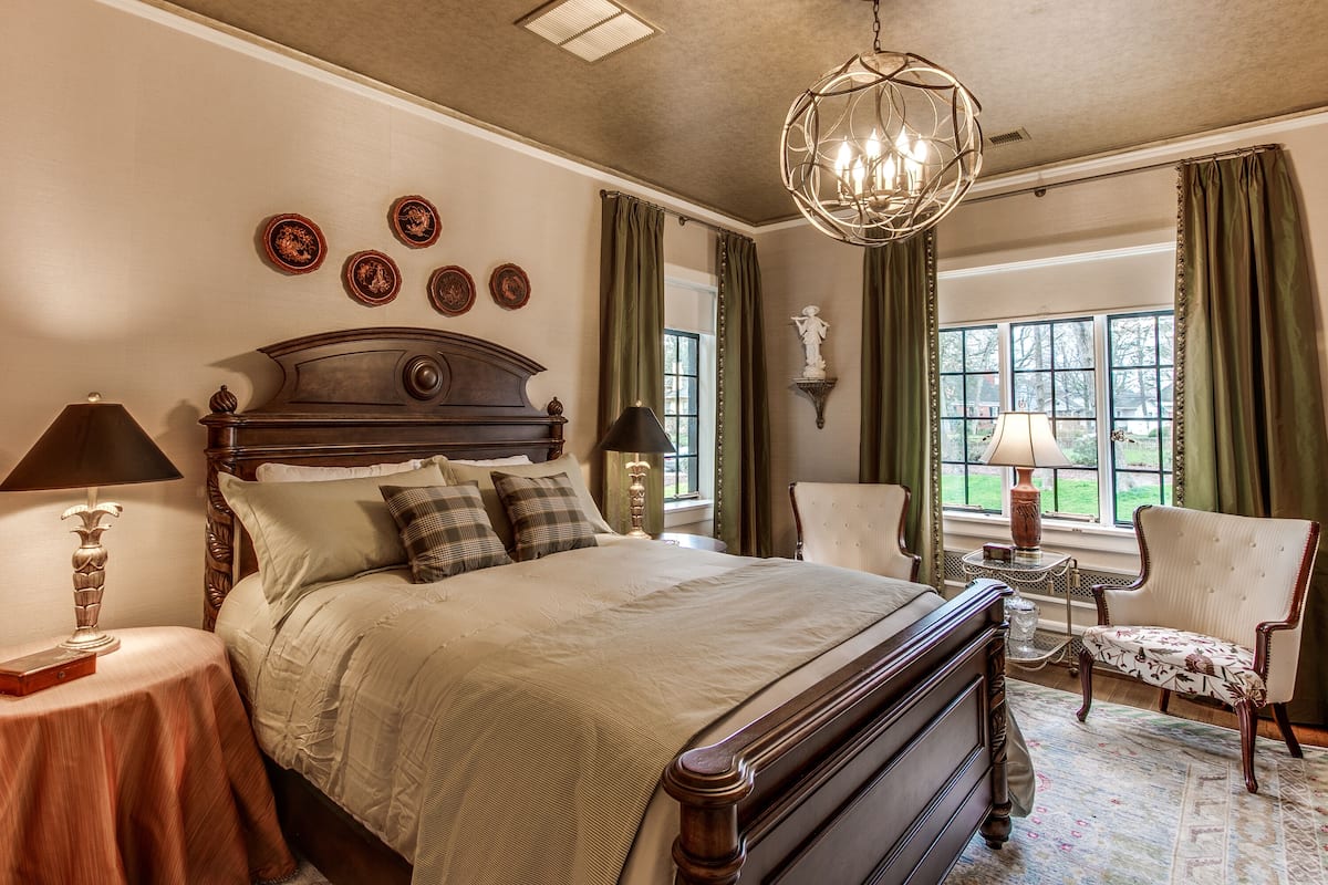 A bedroom with a large bed, two bedside tables with lamps, a chair, and a chandelier.