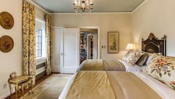 A bedroom with a large bed, floral curtains, a chandelier, and a view of a hallway.