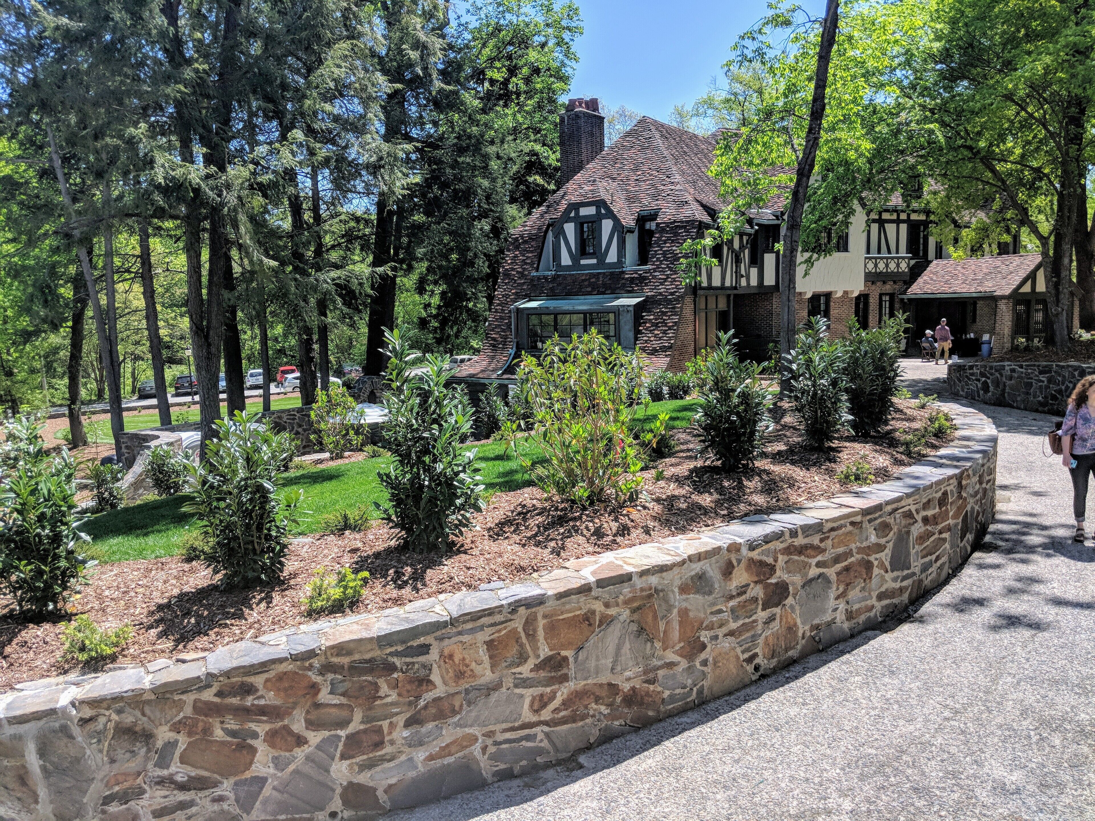 A traditional Tudor-style house with a stone foundation, surrounded by a stone retaining wall and a well-maintained garden.