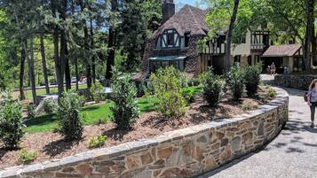 A traditional Tudor-style house with a stone foundation, surrounded by a stone retaining wall and a well-maintained garden.