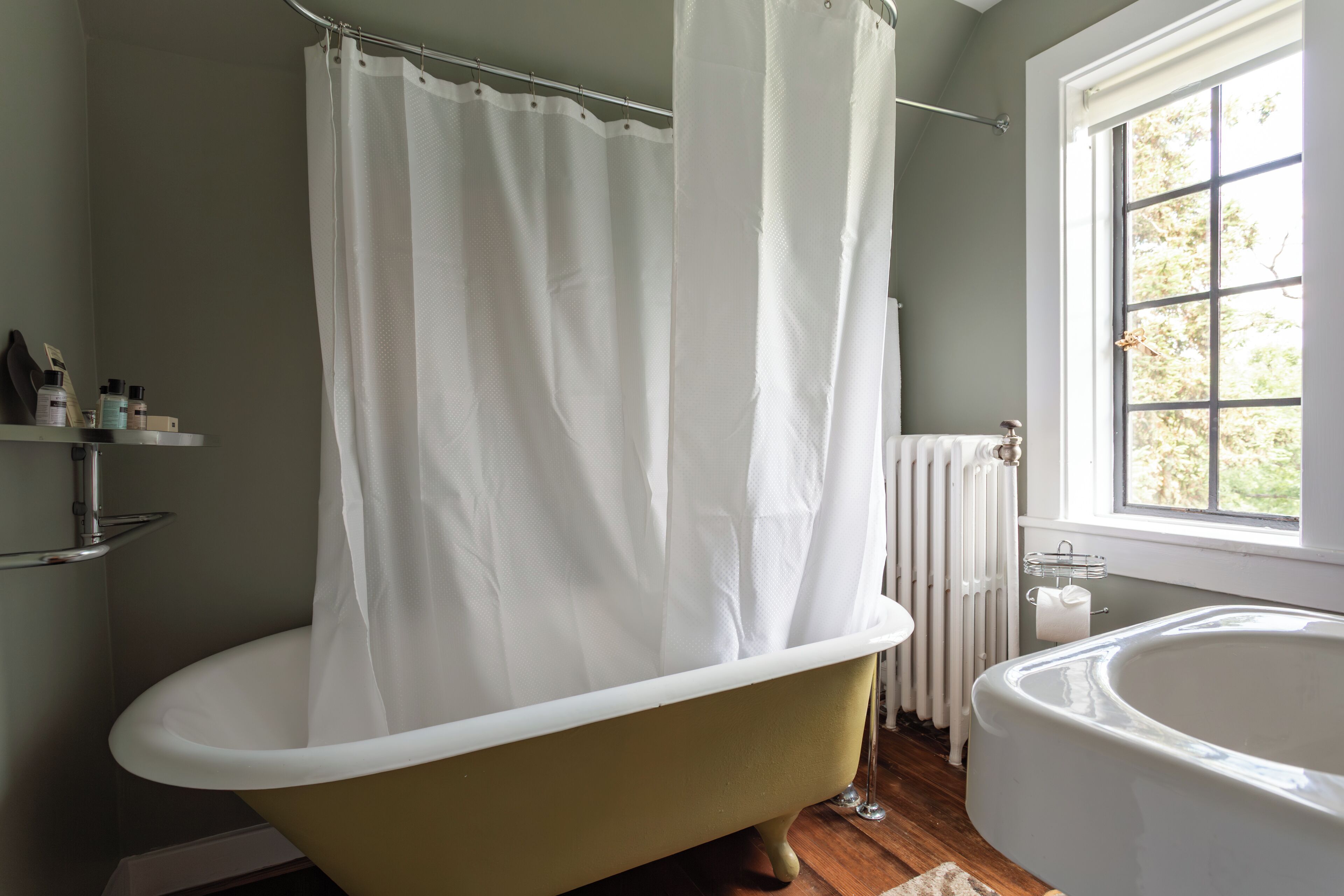A bathroom with a freestanding bathtub, a window with a view of trees, and a radiator.