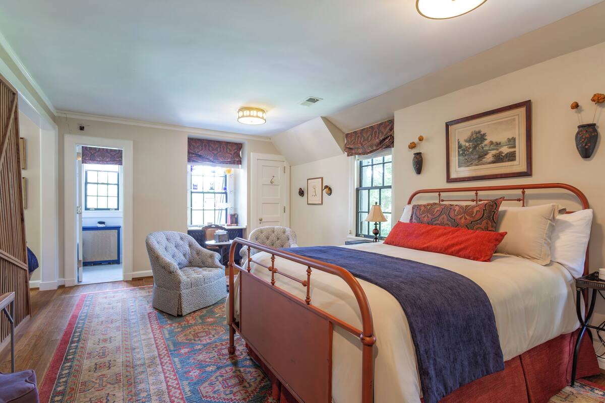 A bedroom with a large bed, a chair, a desk, and a window with curtains.
