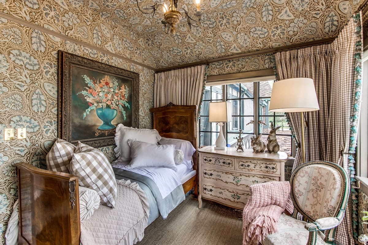 A bedroom with a bed, dresser, chair, and a window with curtains.
