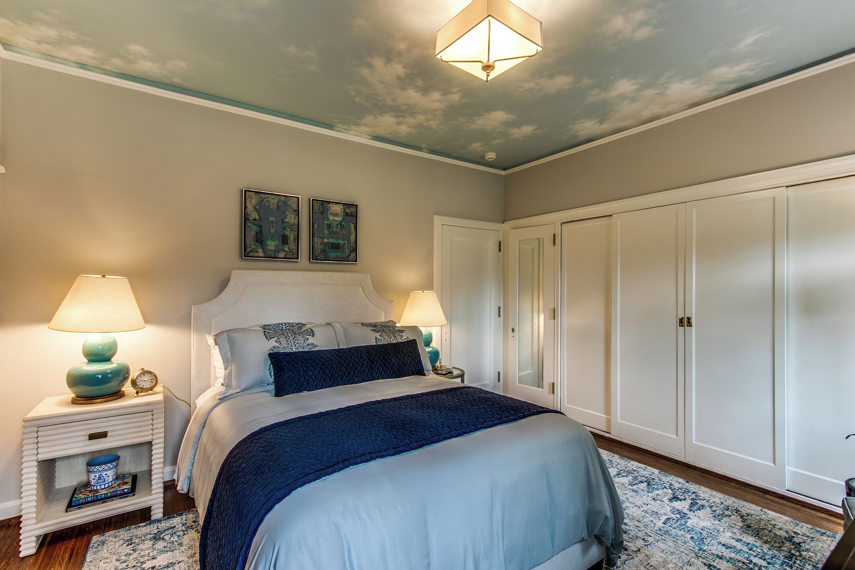 A bedroom with a bed, nightstands, a wardrobe, and a ceiling with a cloud design.