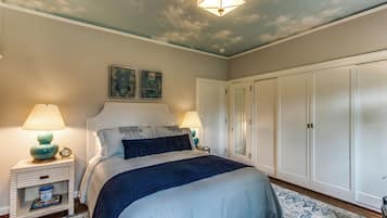 A bedroom with a bed, nightstands, a wardrobe, and a ceiling with a cloud design.