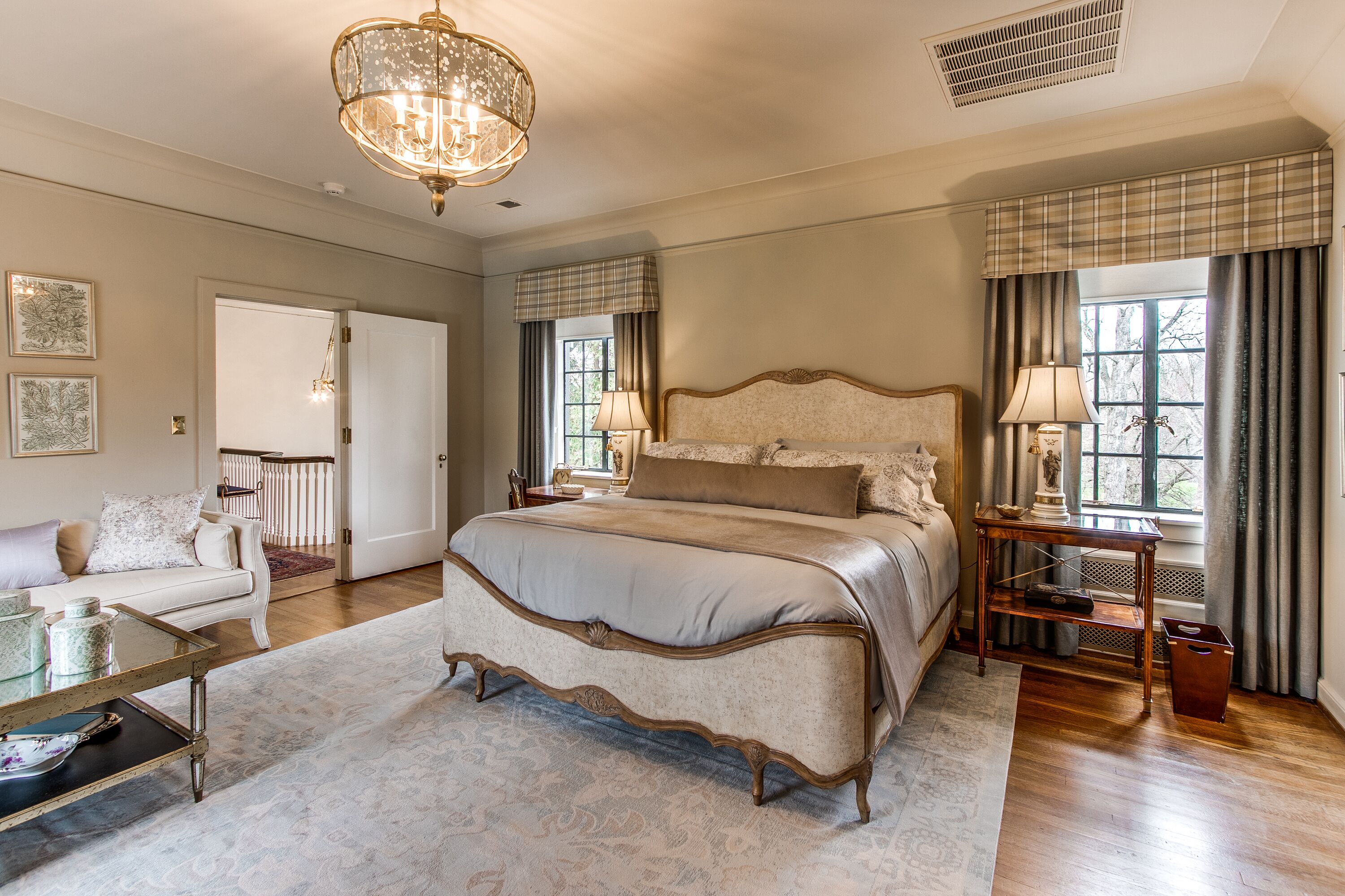 A spacious bedroom with a large bed, a chandelier, a nightstand, and a view of the outdoors.