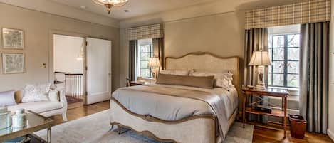 A spacious bedroom with a large bed, a chandelier, a nightstand, and a view of the outdoors.