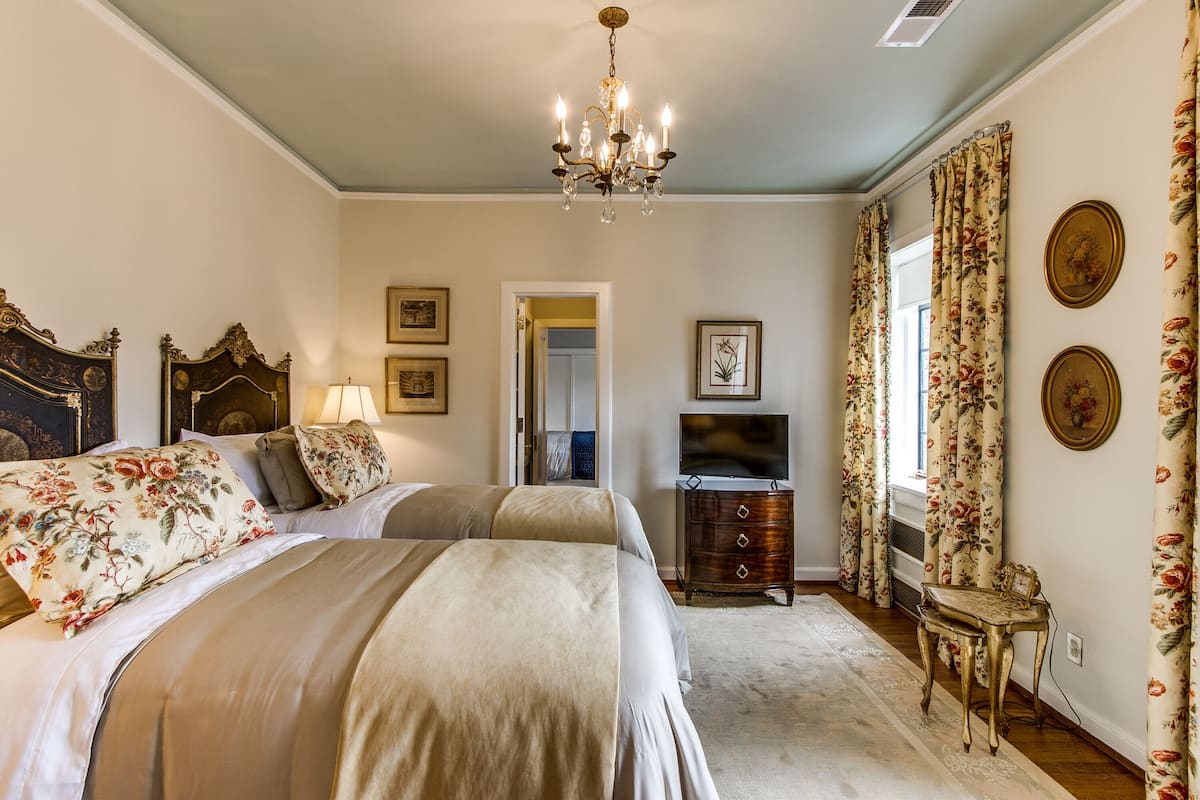 A bedroom with two beds, a chandelier, a dresser, and a television.