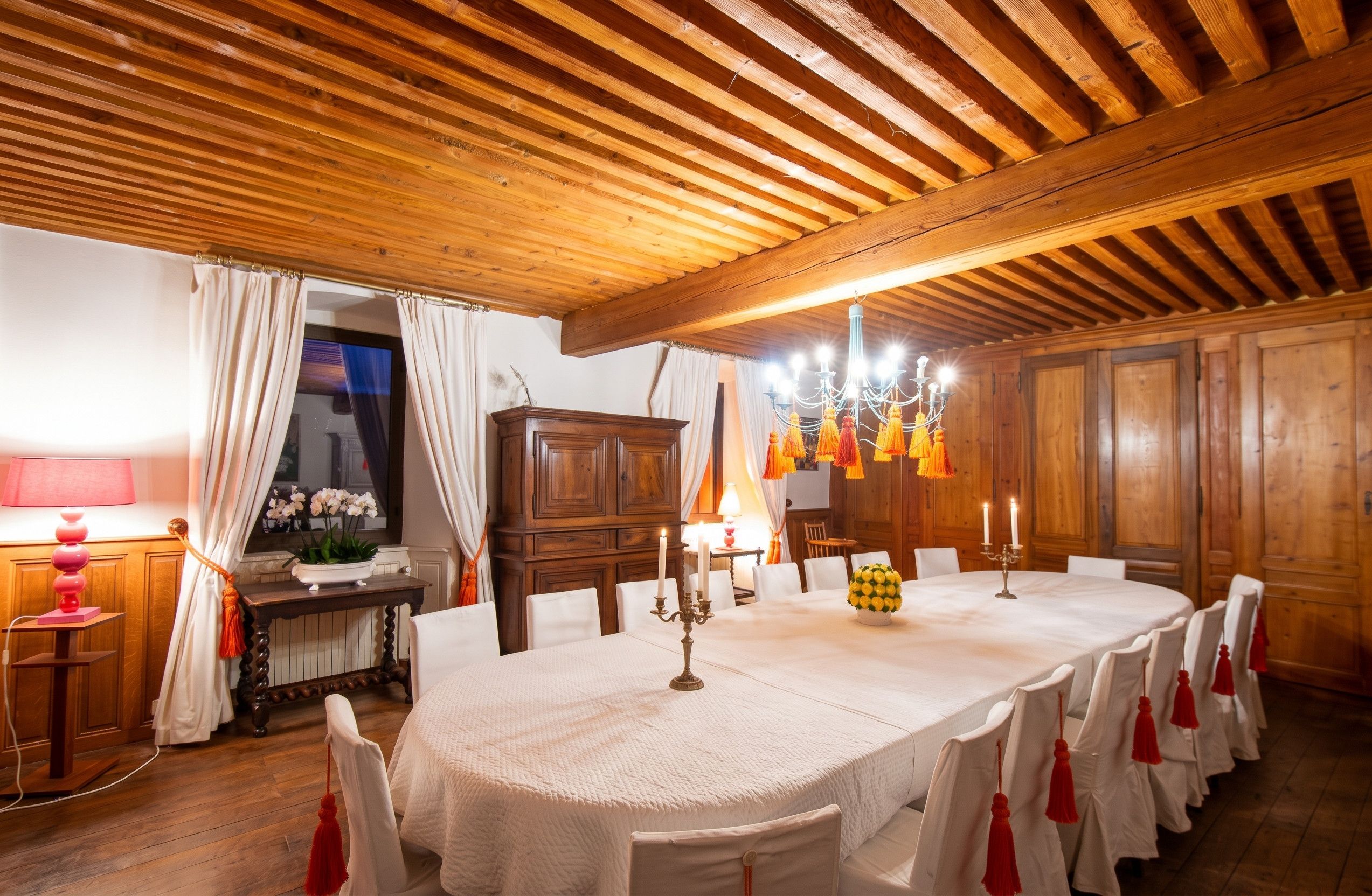 Une salle à manger avec un plafond en bois, un lustre et une table dressée pour le repas.