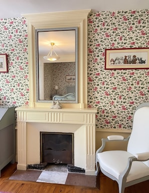 A room with a fireplace, a mirror, floral wallpaper, and a framed picture of dogs. - Homerez - Manor in Satillieu (Satillieu)