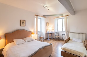 A hotel room with two beds, a small table with a chair, a radiator, and a window with curtains. - Homerez - Manor in Satillieu (Satillieu)