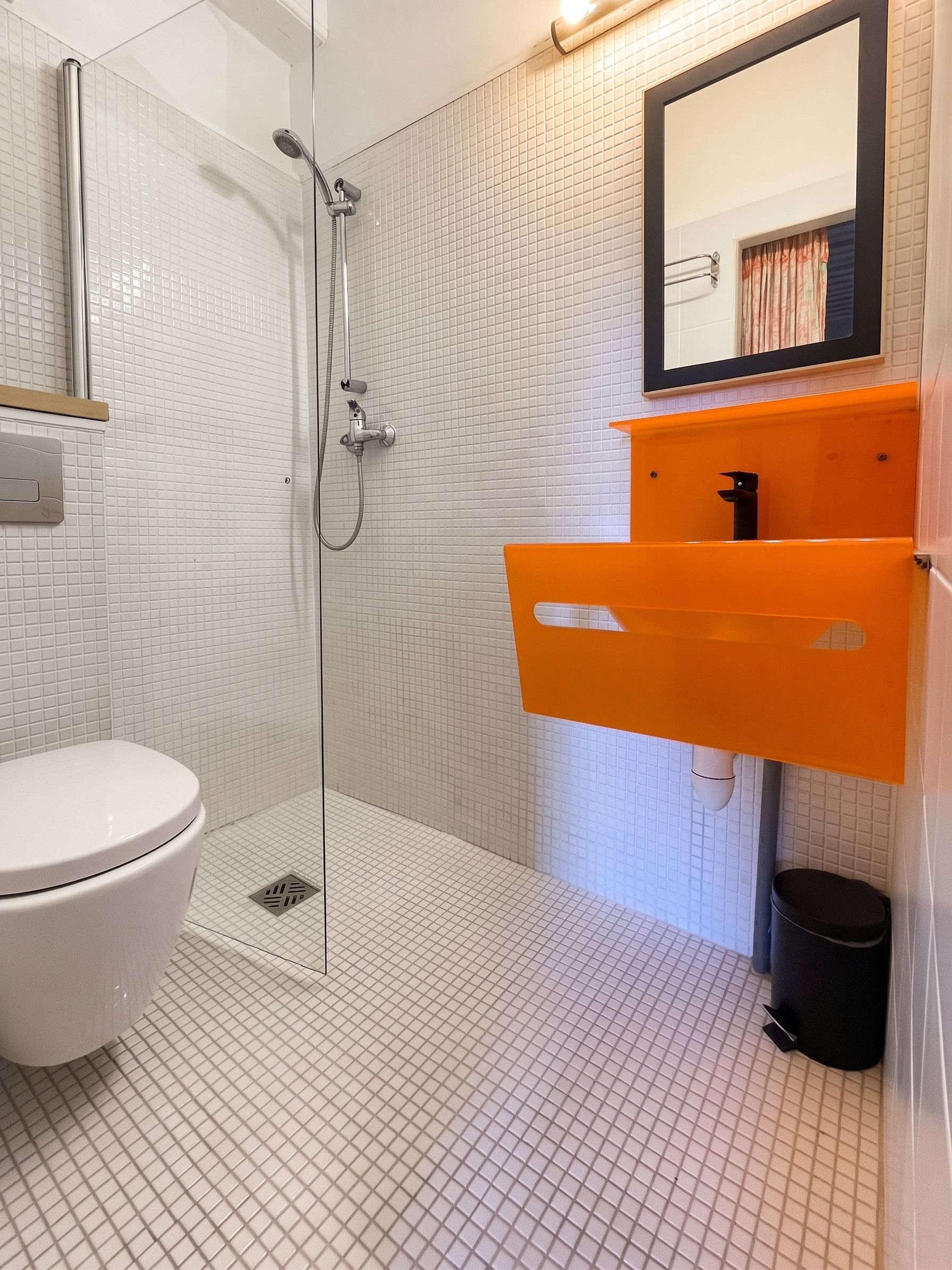A bathroom with a white toilet, a glass-enclosed shower, and an orange sink.