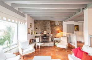 A cozy living room with a stone fireplace, white furniture, and a view through a large window. - Homerez - Manor in Satillieu (Satillieu)