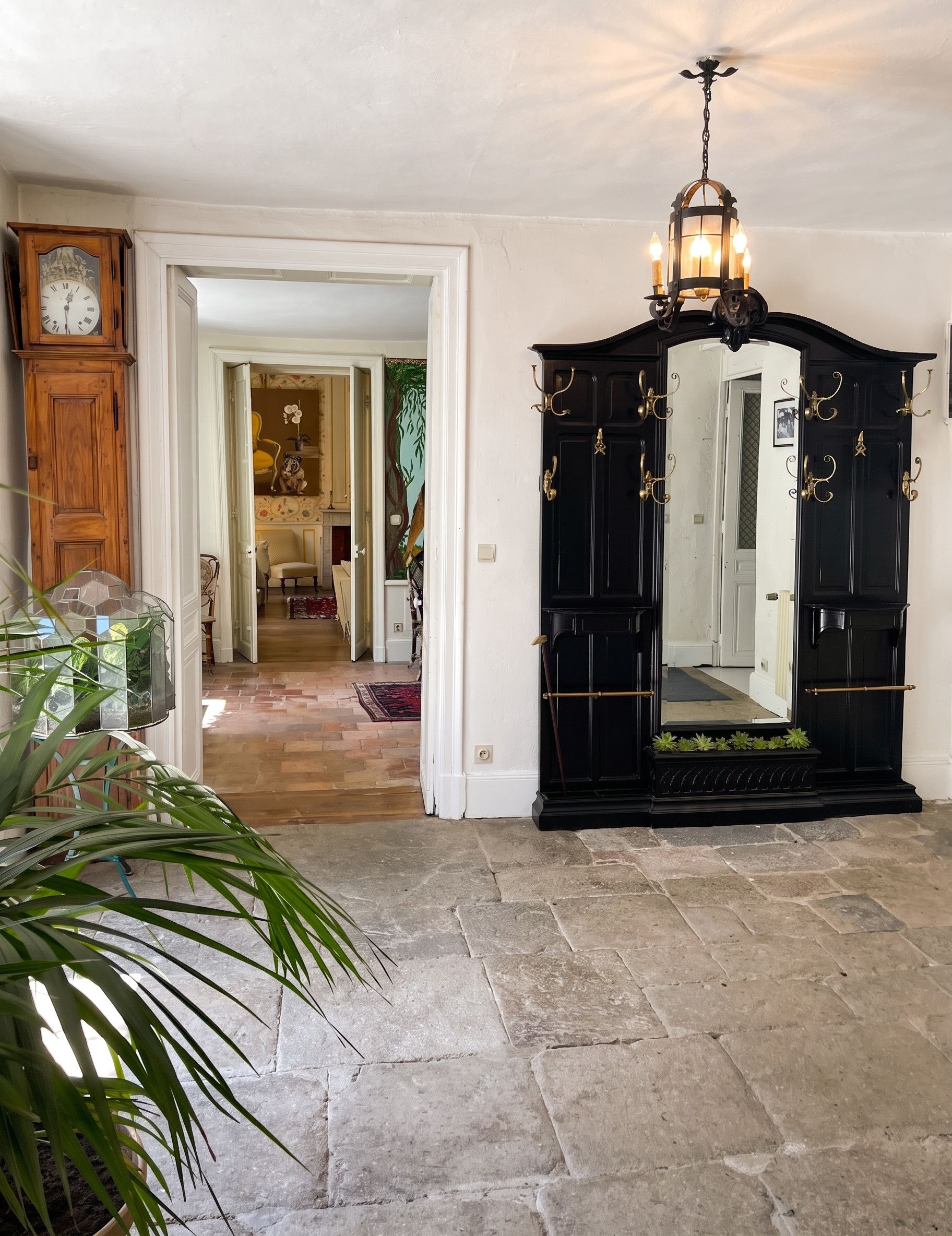 A foyer with a stone floor, a large mirror, a wooden clock, and a chandelier.