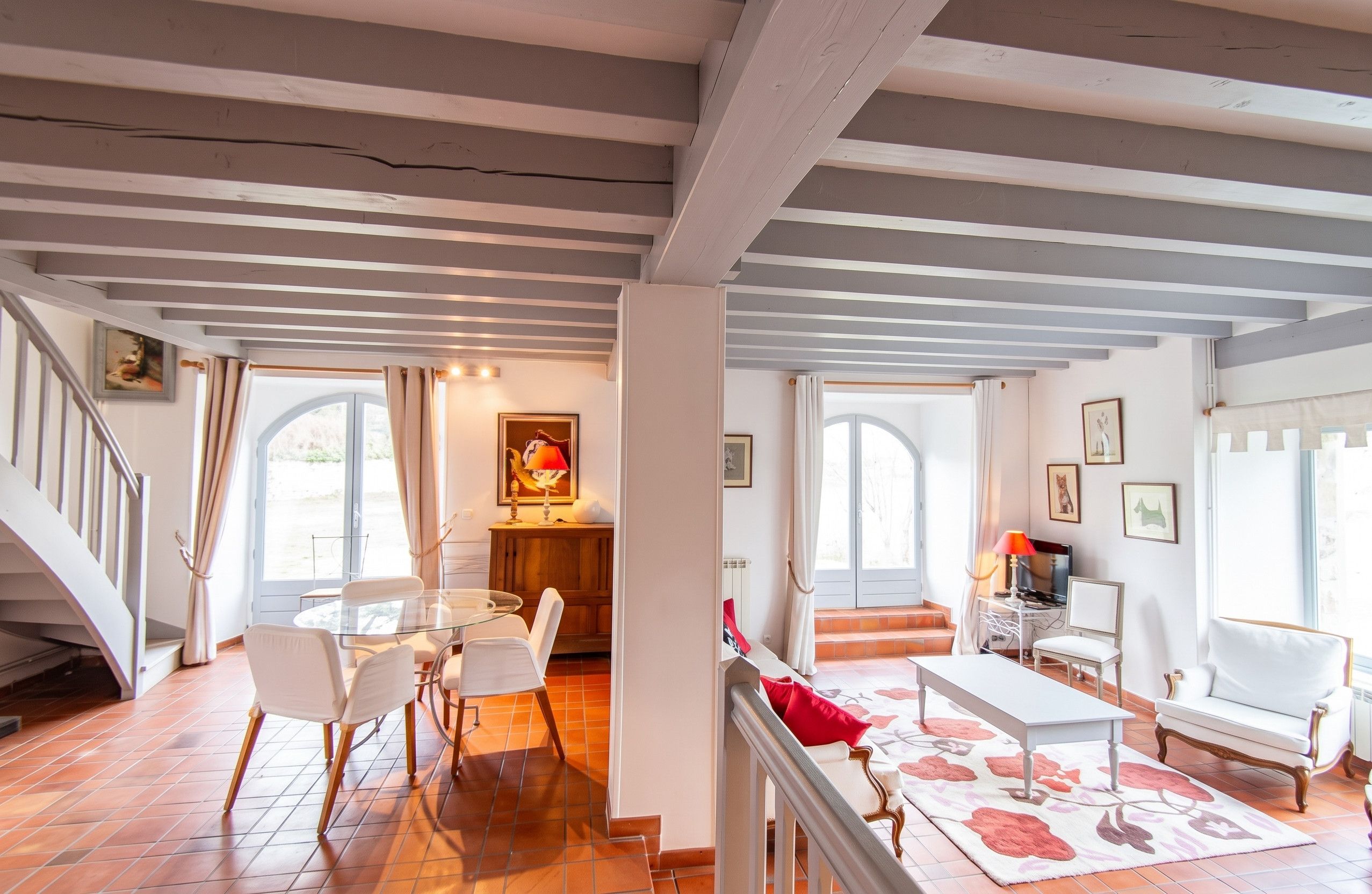 Un grand espace de vie comprenant une table à manger, des chaises, un canapé et un téléviseur. Un escalier mène à un autre niveau.