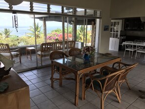 A dining area with a glass table, wicker chairs, and a view of the ocean.