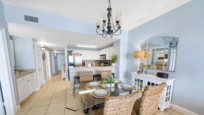 A modern kitchen with white cabinets, a central island, and a dining area with wicker chairs and a glass table.