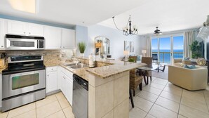 A modern kitchen with a central island, stainless steel appliances, and a dining area with a view of the ocean.