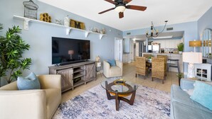 A living room with a TV, sofa, coffee table, and decorative items on shelves.