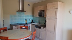 Een kleine keuken met een ronde tafel, stoelen, een magnetron, een spoelbak en kastjes.