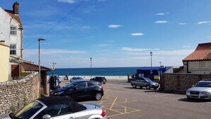 A coastal street with parked cars, a beach in the background, and a sign for a hotel. - Crab Cottage - sleeps 4 guests  in 2 bedrooms (Sheringham)