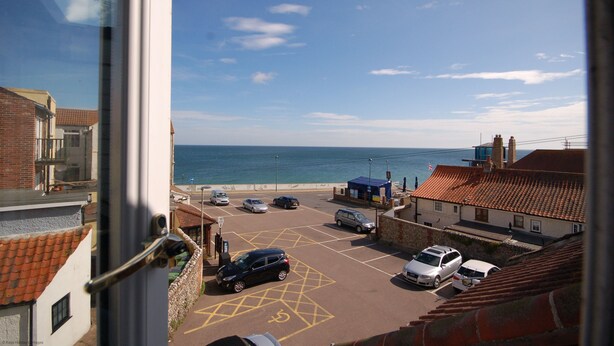 A coastal parking area with cars, a building with a tiled roof, and the sea in the background. - Crab Cottage - sleeps 4 guests  in 2 bedrooms (Sheringham)