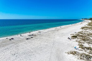 A wide sandy beach with clear blue water, a few people, and some beach chairs. - Sun Plaza West Unit 204, gulf front complex on Ami (Holmes Beach)