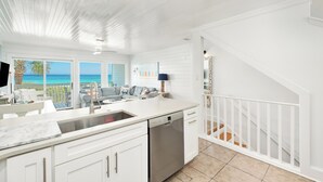 Una cocina moderna con armarios blancos, lavavajillas y vistas al océano.