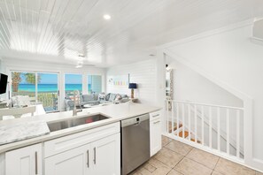 A modern kitchen with white cabinetry, a dishwasher, and a view of the ocean.