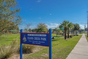 A sign for Egns Creek Park in the City of Fernandina Beach, Florida, with a clear sky and a pathway leading into the park.