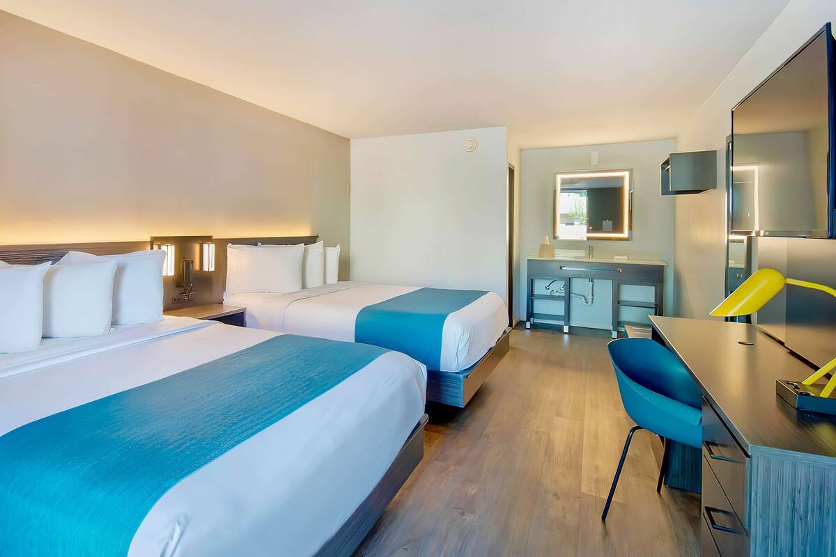 Ein Hotelzimmer mit zwei Betten, einem Schreibtisch, einem Stuhl, einem Spiegel und einem Badezimmer.