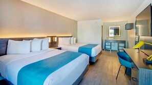 Ein Hotelzimmer mit zwei Betten, einem Schreibtisch, einem Stuhl, einem Spiegel und einem Badezimmer.