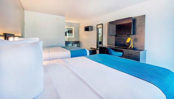 Ein modernes Hotelzimmer mit zwei Betten, einem Schreibtisch, einem Spiegel und einem Fernseher.