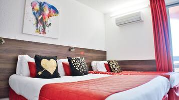 A hotel room with a large bed, a headboard with a wooden finish, a wall-mounted air conditioner, and a window with red curtains.