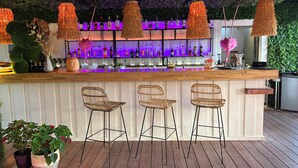 A bar area with a wooden counter, three wicker bar stools, and a variety of bottles and glasses. - Hôtel des 2 golfs (Leucate)