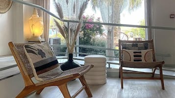Una habitación con dos sillones de mimbre, un pequeño reposapiés blanco y una estatua de Buda.