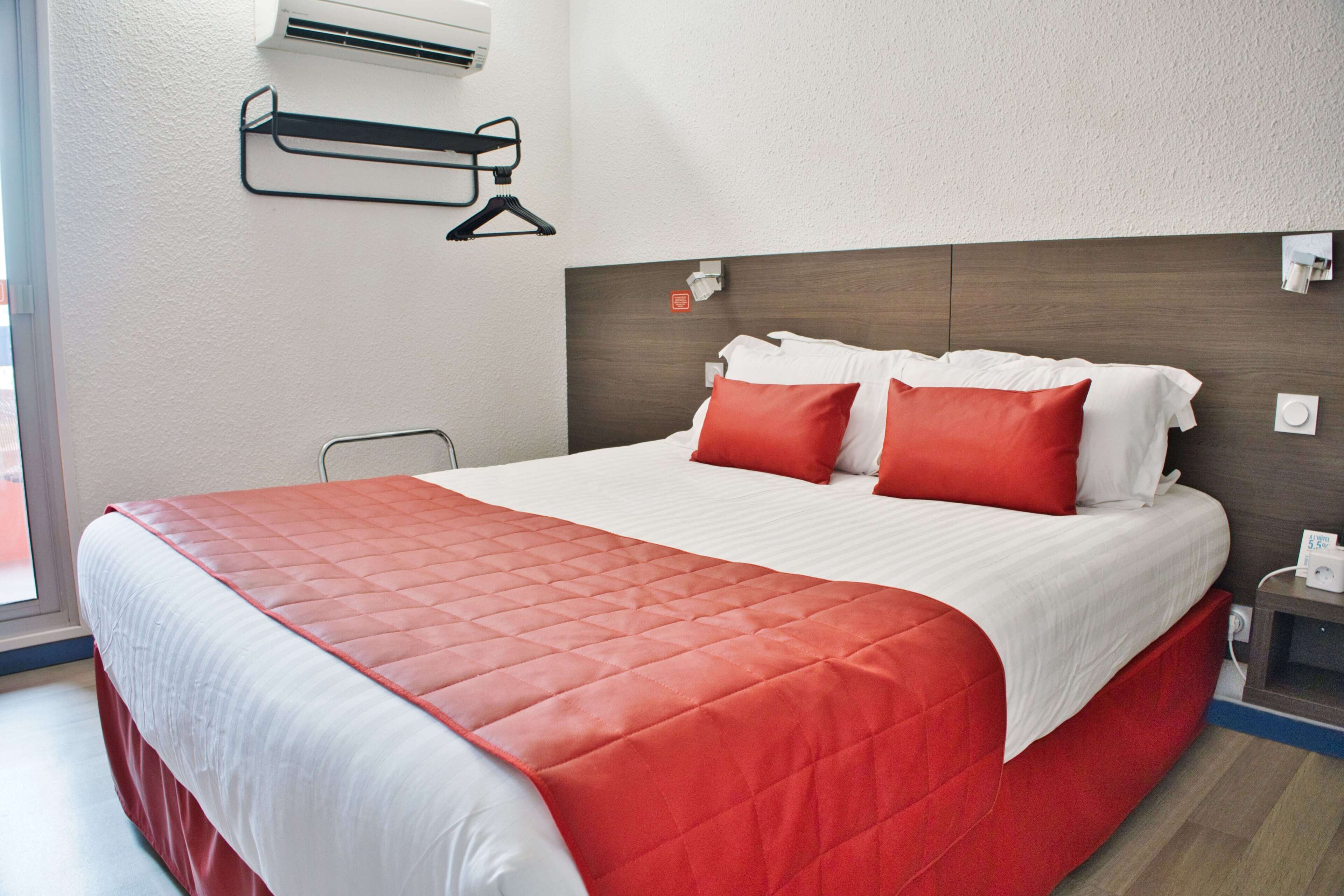 A neatly made bed with a red and white bedspread, a wooden headboard, and a bedside table with a lamp and phone.