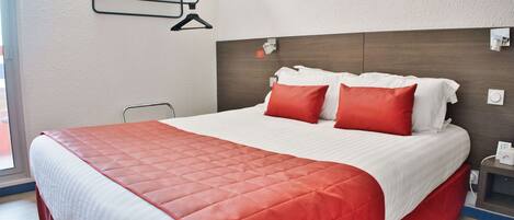 A neatly made bed with a red and white bedspread, a wooden headboard, and a bedside table with a lamp and phone.