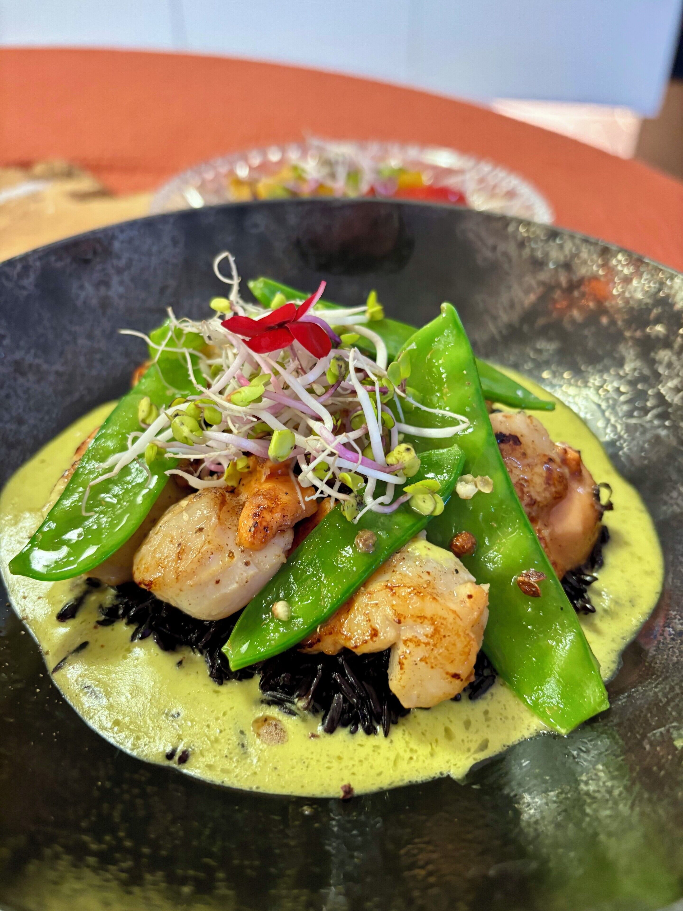 Un piatto con capesante scottate, verdure verdi e germogli.