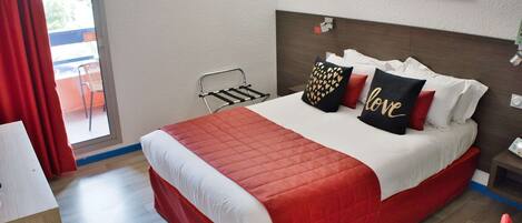 A hotel room with a large bed, a small table, a chair, a window with curtains, and a painting on the wall.