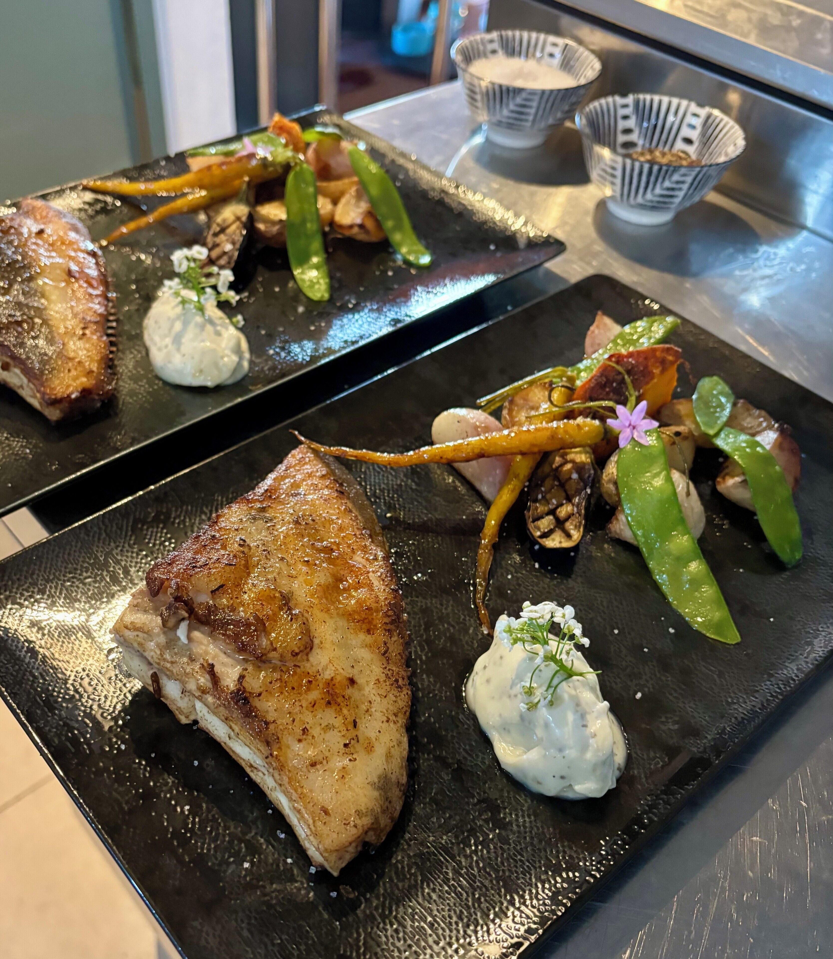 Un plateau de service noir en ardoise, sur lequel on trouve un plat de viande grillée, des légumes verts et une cuillerée de sauce blanche.