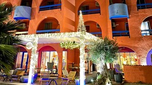 A multi-story building with a warm orange facade, multiple balconies, and a covered outdoor seating area with chairs and tables. - Hôtel des 2 golfs (Leucate)