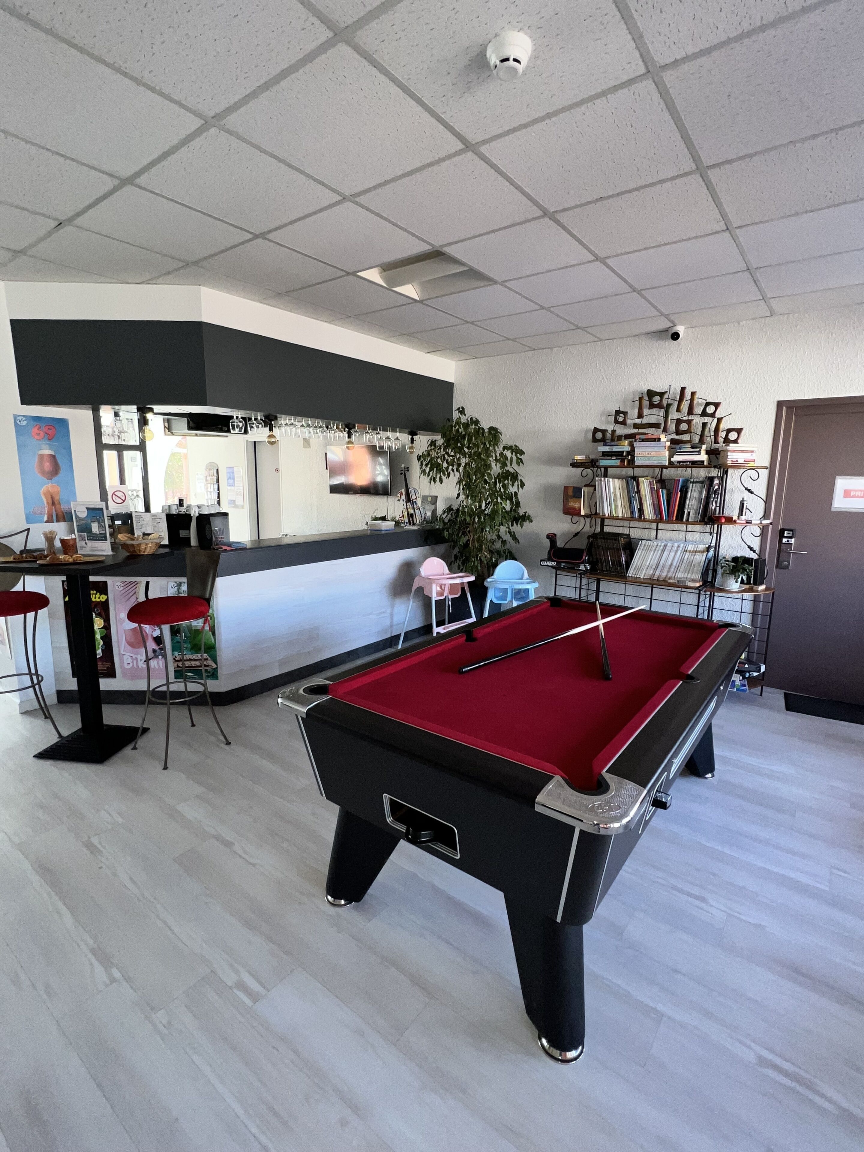 A pool table in a room with a bar area, chairs, and a bookshelf.