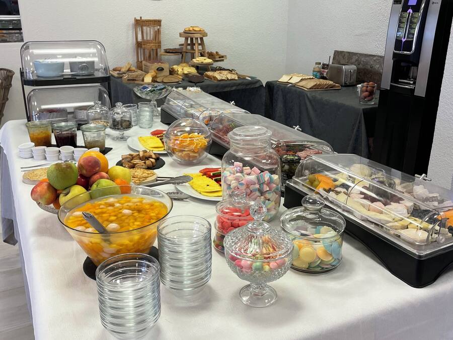 Una mesa de buffet con diversos alimentos y bebidas, incluyendo frutas, pastelería y una máquina de café.
