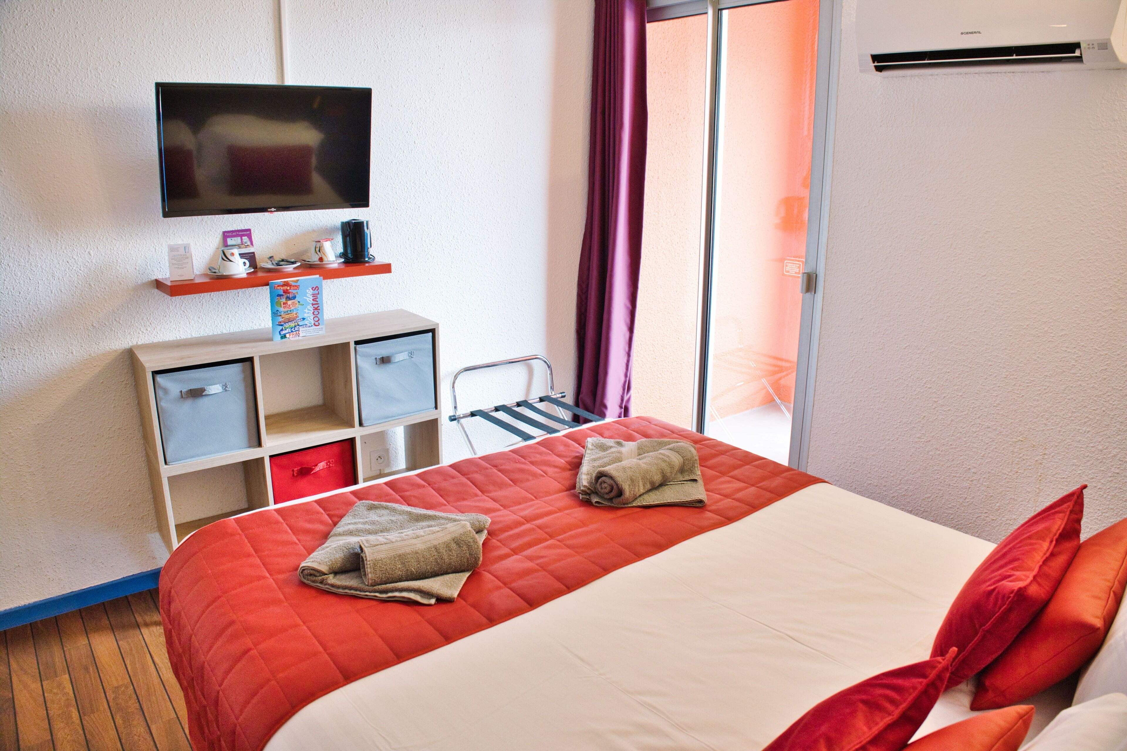 A hotel room with a bed, a TV, a desk with drawers, a chair, and a window with curtains.