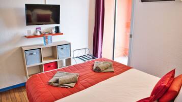 A hotel room with a bed, a TV, a desk with drawers, a chair, and a window with curtains.